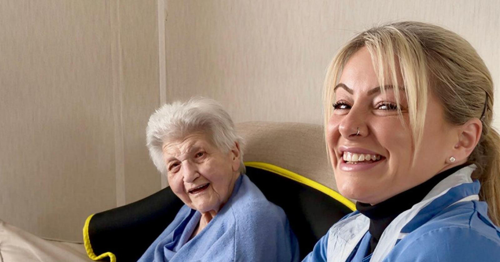 A smiling Anchusa Care carer sitting beside a happy lady in her own home