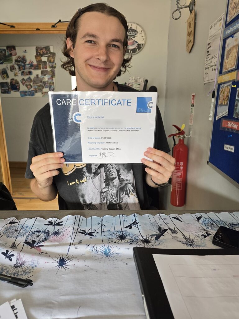 A smiling member of the Anchusa Care team holding up his Care Certificate
